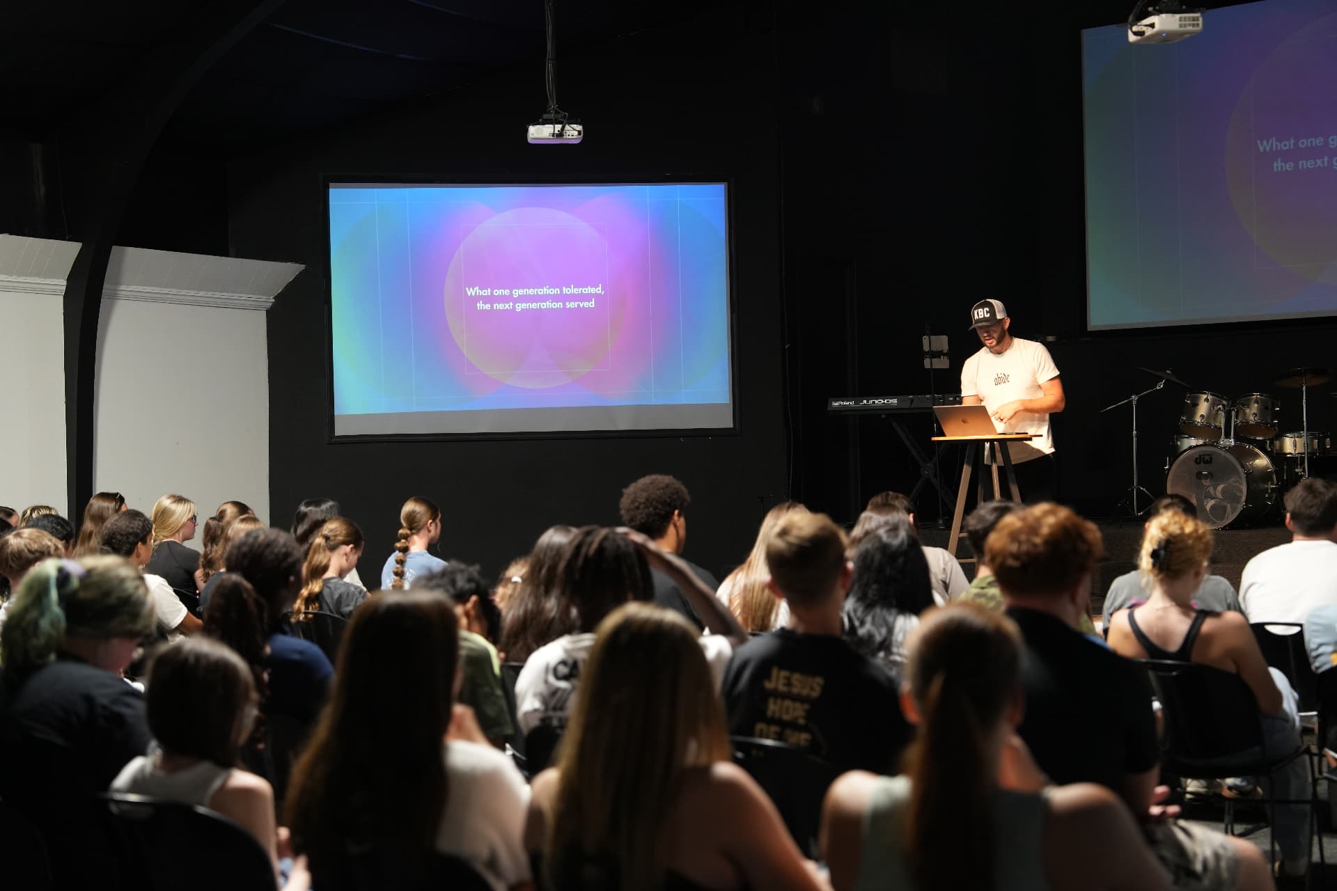 Wide shot of Cody preaching to a room of students